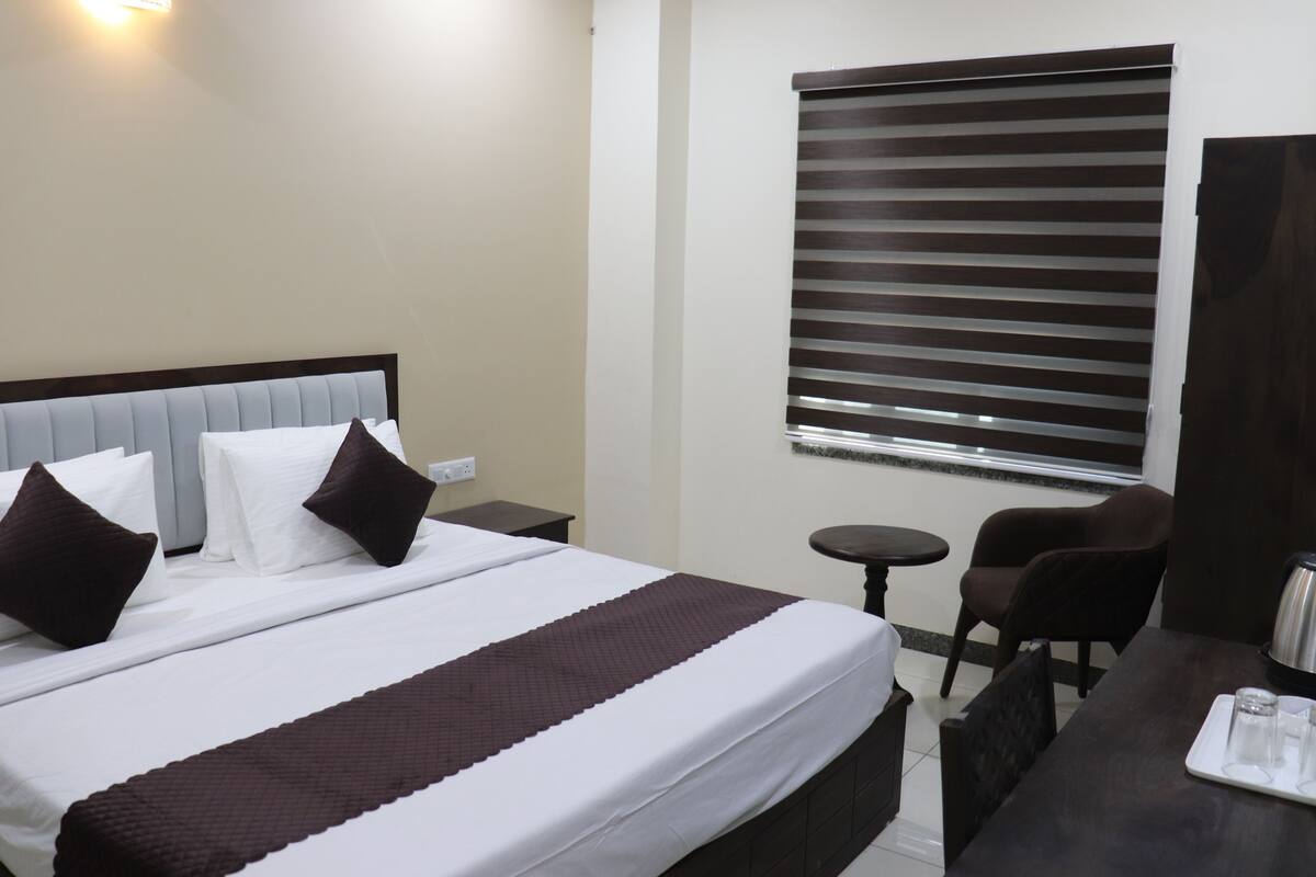 A hotel room with a bed, a small table with a tray, a chair, and a window with blinds.
