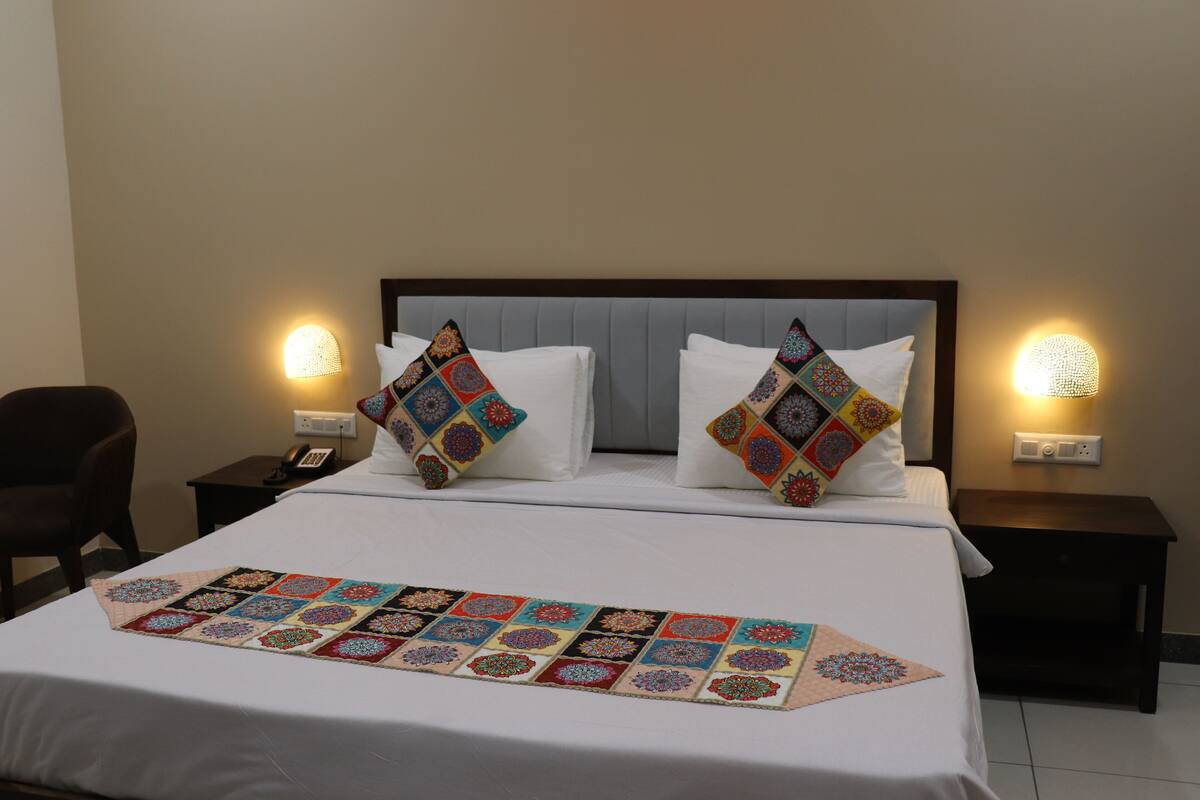 A neatly made bed with a colorful quilt and two decorative pillows, flanked by bedside tables with lamps.