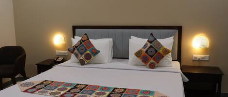 A neatly made bed with a colorful quilt and two decorative pillows, flanked by bedside tables with lamps.