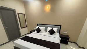 Habitación de hotel ordenada con una cama grande, una mesita de noche, una lámpara de pared y una puerta.