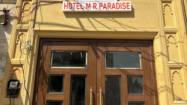 Entrada de hotel con un cartel que dice "HOTEL M R PARADISE" y un logotipo encima.