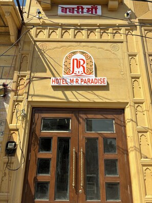 Entrada de hotel con un cartel que dice "HOTEL M R PARADISE" y un logotipo encima.