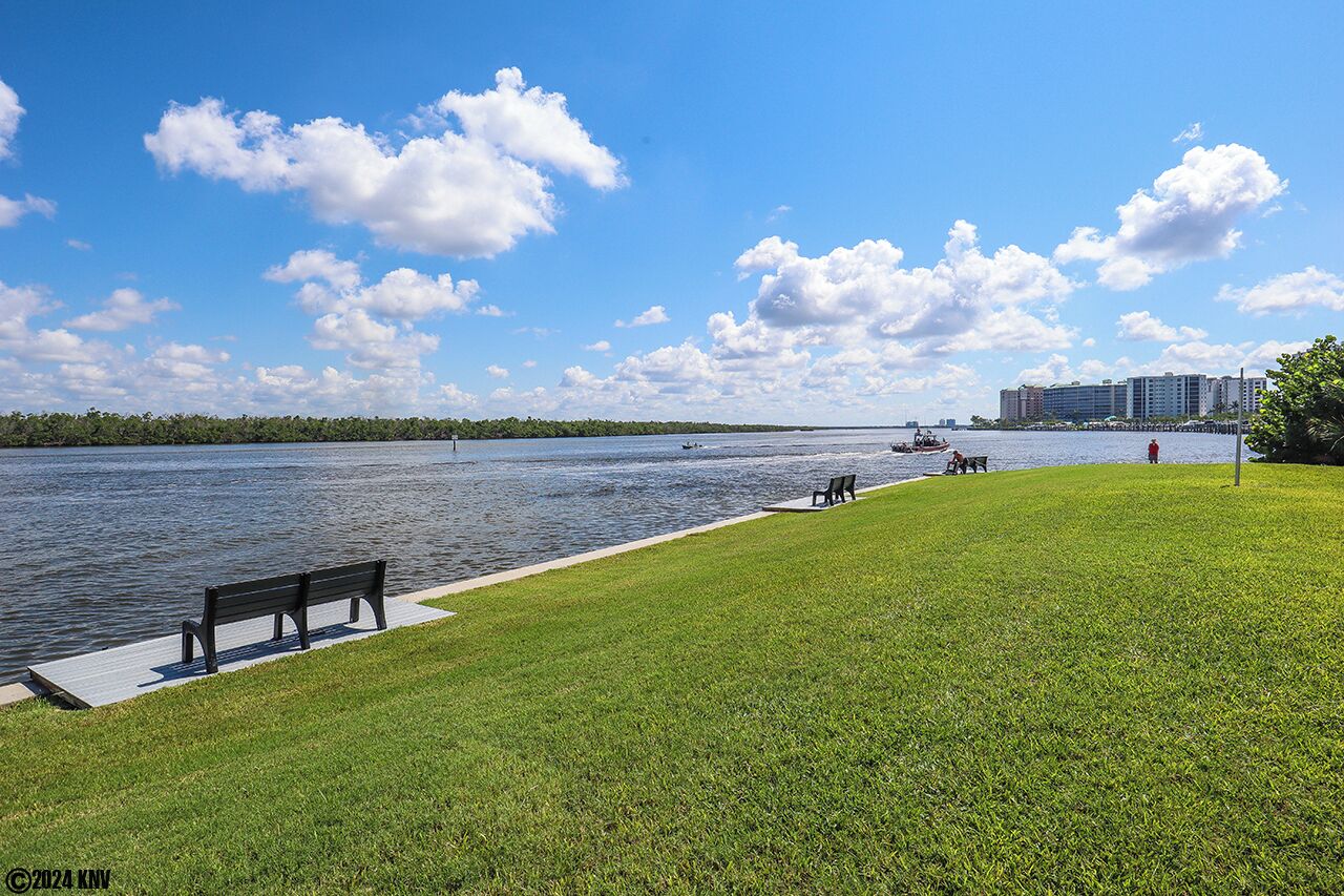 Un parc au bord de l’eau, avec une pelouse, un banc et une promenade le long du rivage.