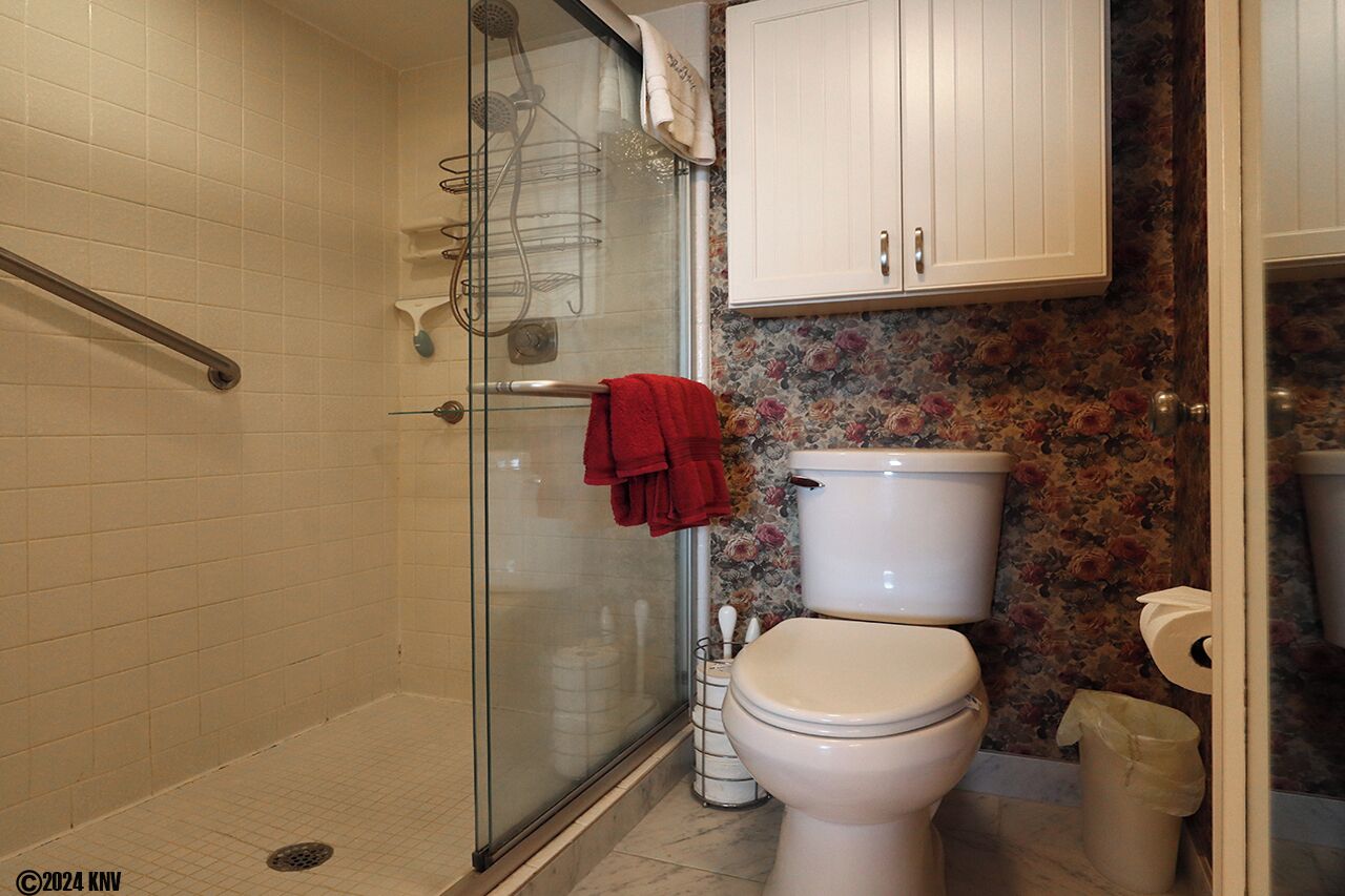 A bathroom with a glass shower enclosure, a toilet, and a sink.