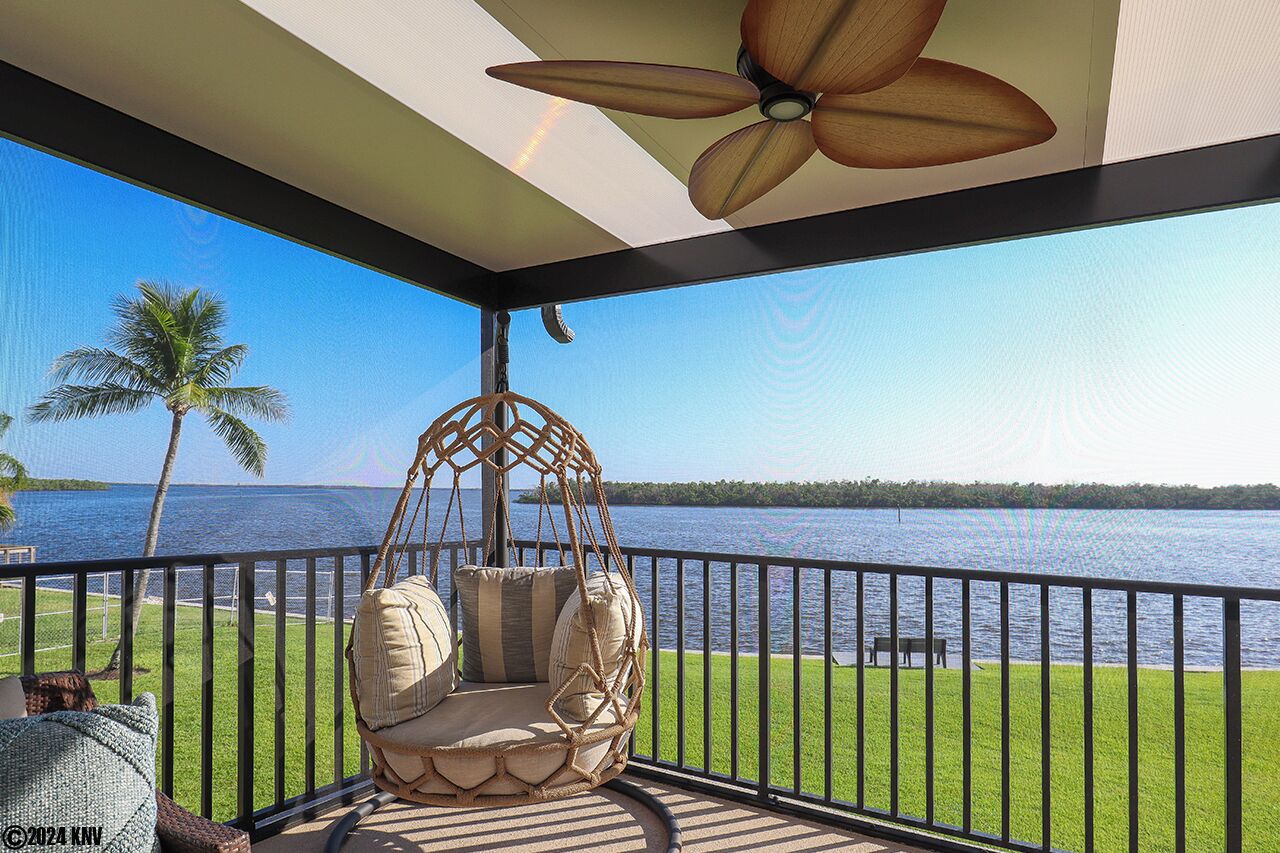 A balcony with a hanging chair, a ceiling fan, and a view of a lake.