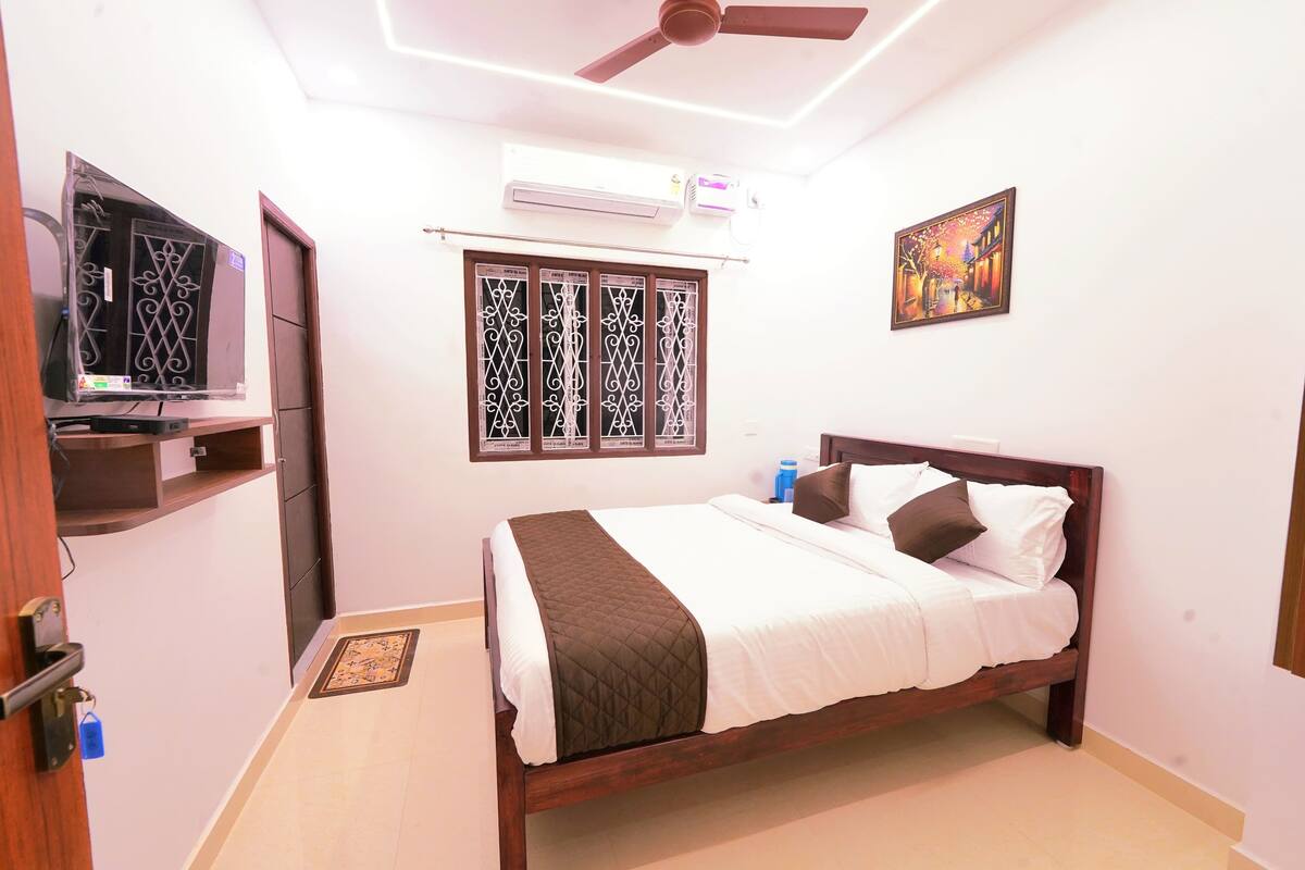 A bedroom with a bed, a ceiling fan, an air conditioning unit, a window with decorative grills, and a wall-mounted painting.