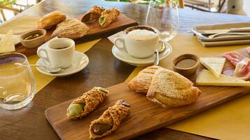 A wooden table with pastries, coffee cups, and a cheese board.