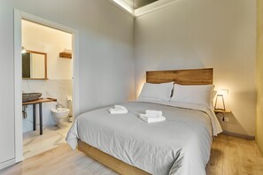 A modern bedroom with a large bed, a wooden headboard, a bedside table with a lamp, and a bathroom with a sink and mirror. - Hotel Ristorante La Dama nella Vigna  (Monteriggioni)