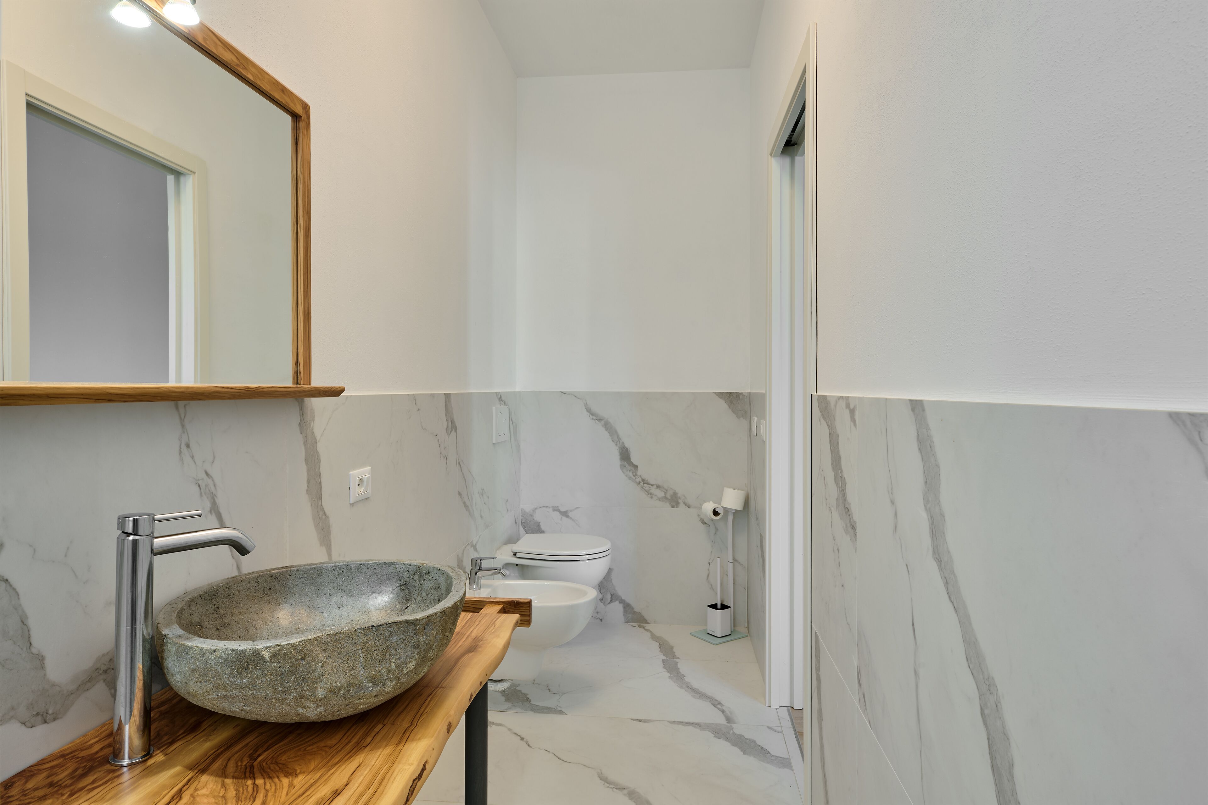 Ein Badezimmer mit einem Steinkonstruktion als Waschbecken, einem modernen Wasserhahn, einer Toilette und einer Marmorwand.