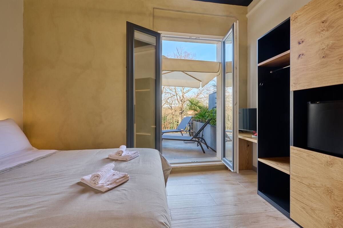 A modern hotel room with a bed, a large sliding glass door leading to an outdoor area, and built-in wooden shelving.