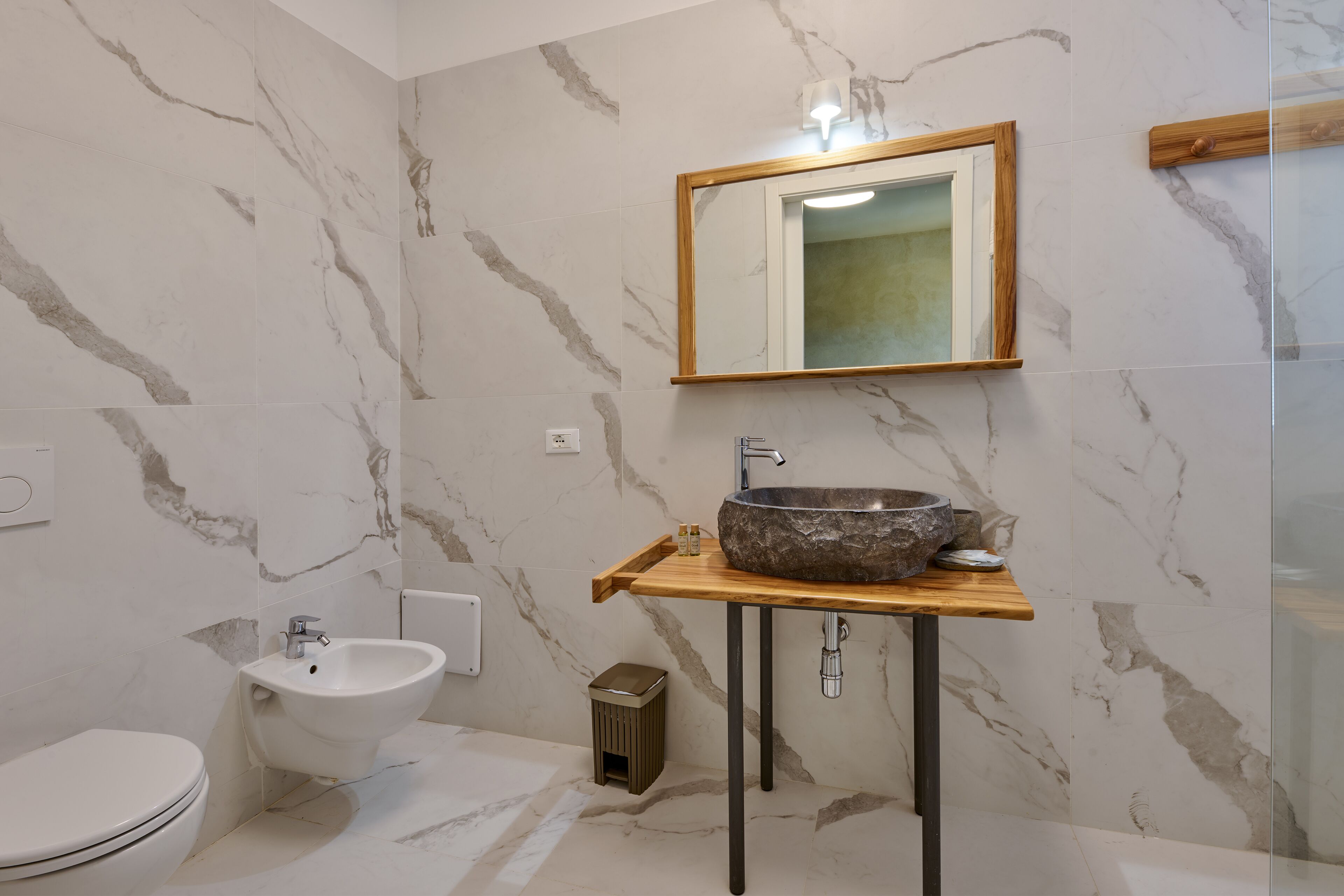 Ein Badezimmer mit Marmorwand, einem Holzlagerraum, einem weißen Waschbecken, einem Bidet und einem Spiegel.