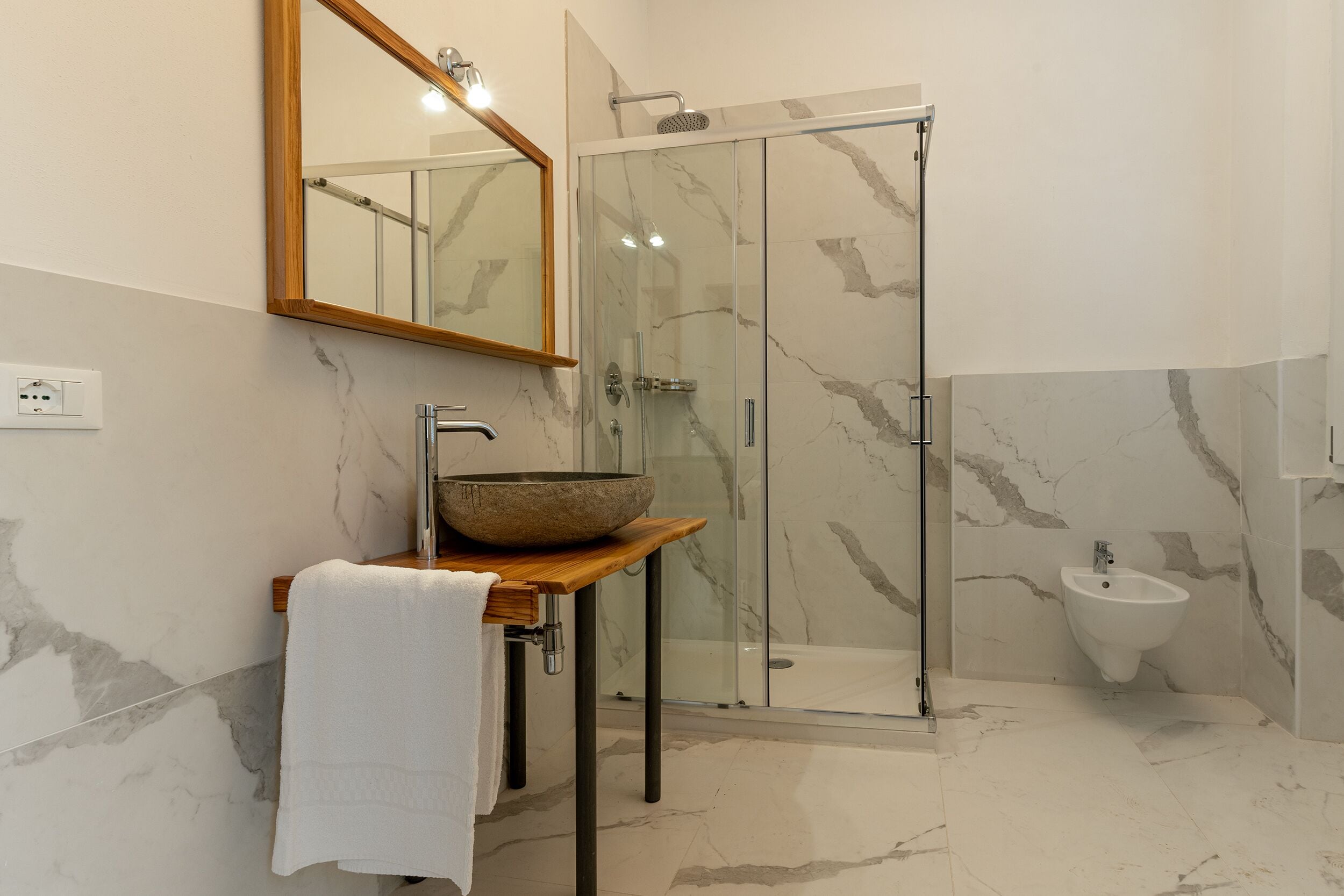 Une salle de bain avec un lavabo en marbre, un meuble-lavabo en bois, une cabine de douche en verre et un bidet.