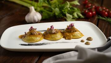 A white rectangular plate with three dumplings topped with a sauce and garnished with purple flowers, placed on a wooden table.