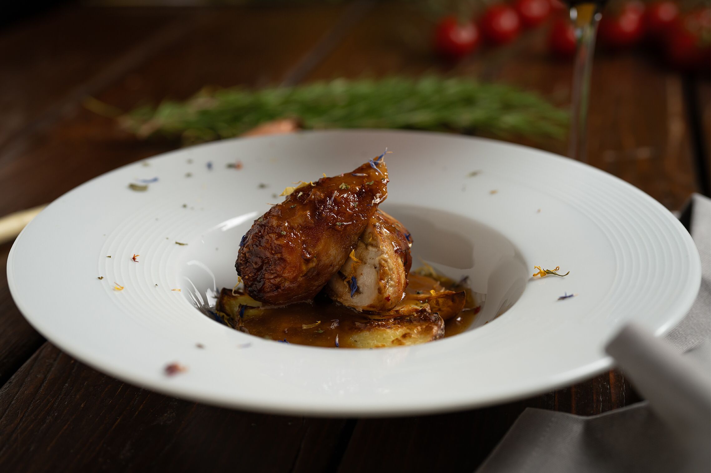 A white plate with a roasted chicken leg and sauce on a wooden table.