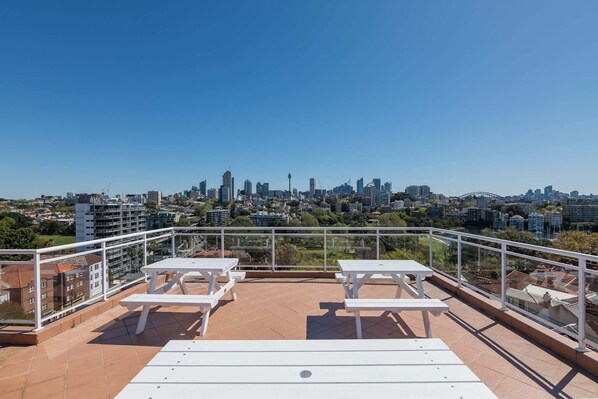 A rooftop terrace with white tables and chairs, offering a panoramic view of a city skyline. - Delightful Darling Point Studio w Stunning Rooftop (Darling Point)