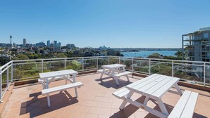 A rooftop terrace with white picnic tables and a city view. - Delightful Darling Point Studio w Stunning Rooftop (Darling Point)