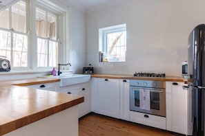 Cucina con pensili bianchi, piano di lavoro in legno, piano cottura a gas, forno e frigorifero.