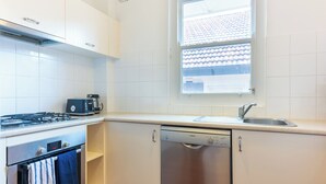A kitchen with white cabinets, a Bosch dishwasher, a stove, and a window with a view of a tiled roof.