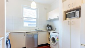 A compact kitchen with a dishwasher, washing machine, microwave, and a window providing natural light.