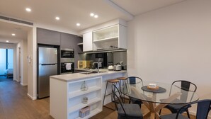 Una cocina moderna con una isla central, electrodomésticos integrados y una zona de comedor con mesa y sillas de vidrio.