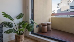 Eine moderne Wohnung mit einem großen Schiebe-Glasfenster, das auf einen Balkon führt. Innen befindet sich ein Blumentopf, ein gewebter Korb und ein kleiner Holzschemel.