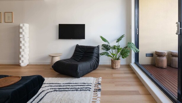 Ein modernes Wohnzimmer mit einem schwarzen Sofa, einem Flachbildfernseher, einer Topfpflanze und Holzboden.