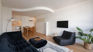 Ein modernes Wohnzimmer mit einer schwarzen Couch, einem schwarzen Sessel und einem Essbereich mit Holztisch und Stühlen.