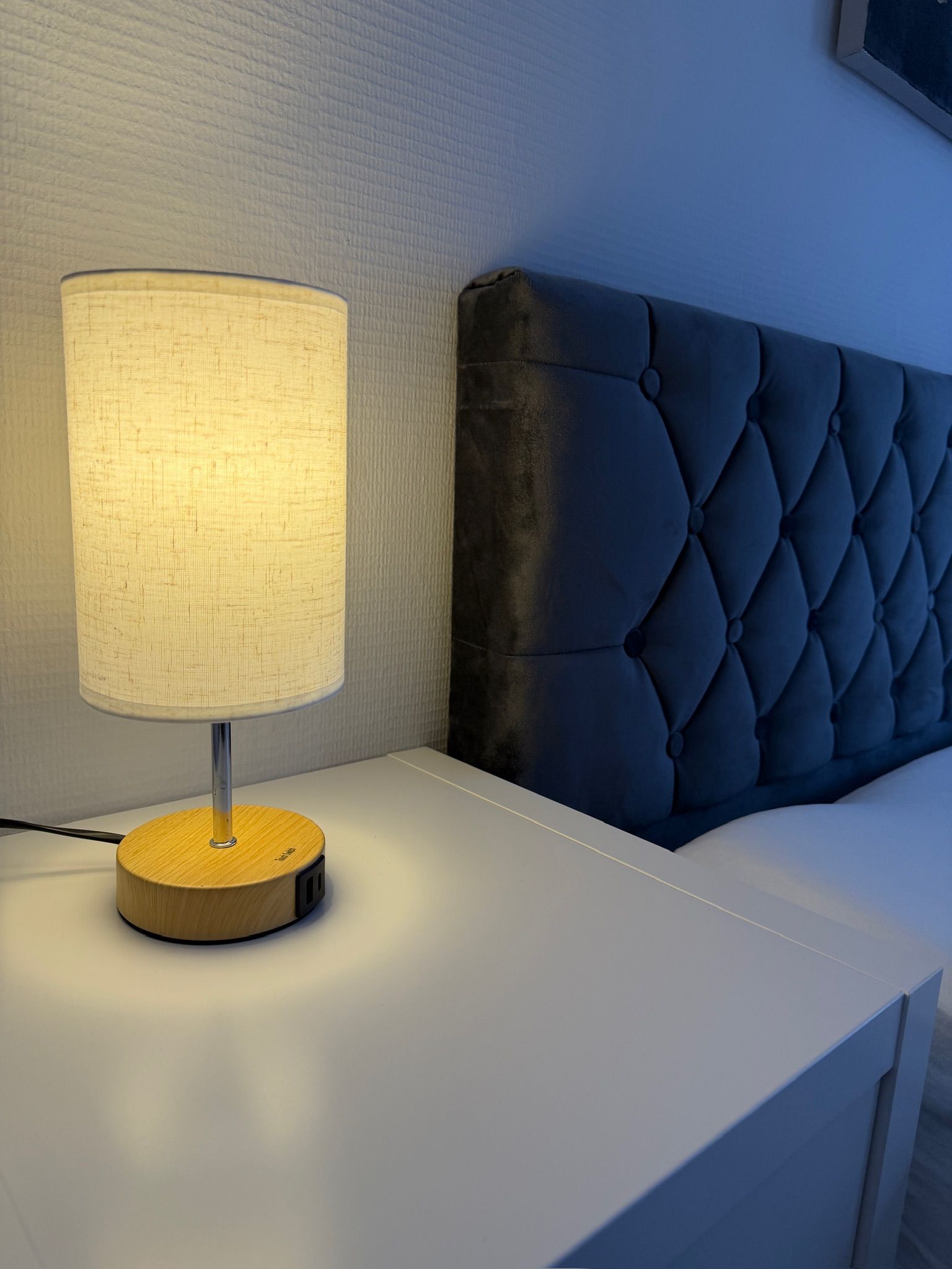 A bedside table with a lamp and a tufted headboard.