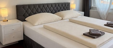 A hotel room with a large bed, two bedside tables, a wall-mounted artwork, and a window with curtains.