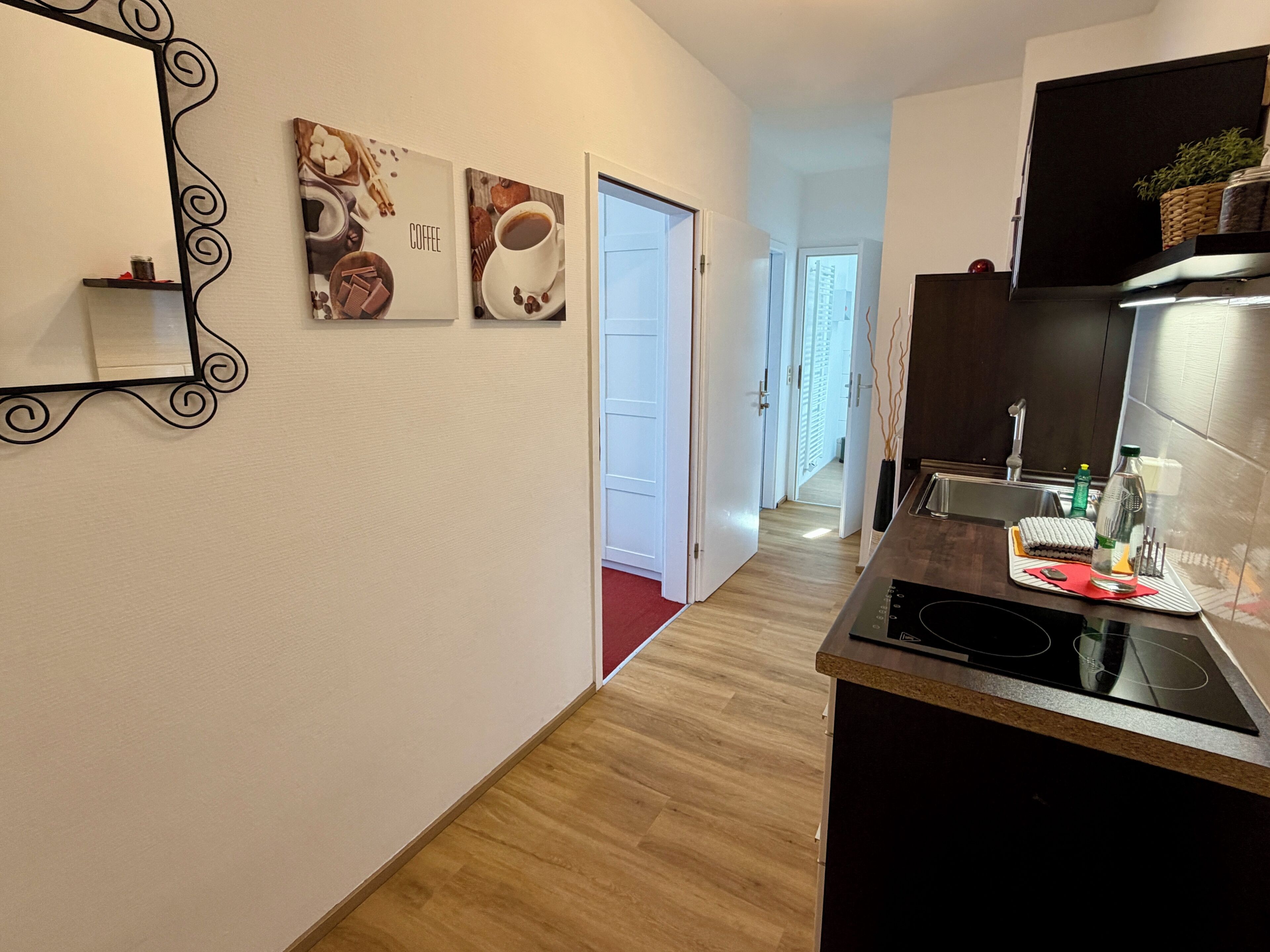 Eine moderne Küche mit schwarzem Arbeitsplatz, einer Edelstahlspüle und einer schwarzen Induktionskochplatte. An der Wand hängen zwei Bilder: eines zeigt Kaffee, das andere Gebäck.
