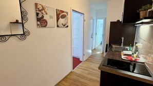 A modern kitchen with a black countertop, a stainless steel sink, and a black induction cooktop. There are two framed pictures on the wall, one depicting coffee and the other pastries.
