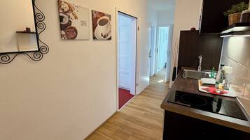 Eine moderne Küche mit schwarzem Arbeitsplatz, einer Edelstahlspüle und einer schwarzen Induktionskochplatte. An der Wand hängen zwei Bilder: eines zeigt Kaffee, das andere Gebäck.