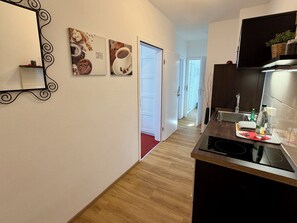 A modern kitchen with a black countertop, a stainless steel sink, and a black induction cooktop. There are two framed pictures on the wall, one depicting coffee and the other pastries.