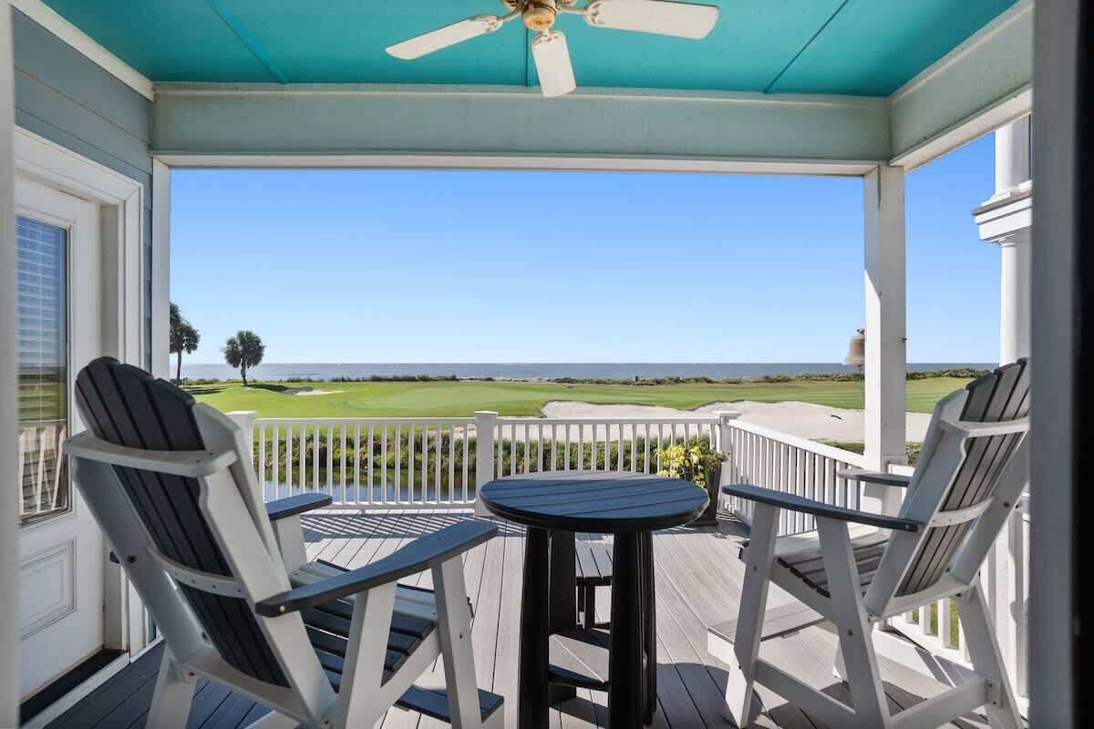A covered outdoor area with a table and chairs, a ceiling fan, and a view of a golf course.