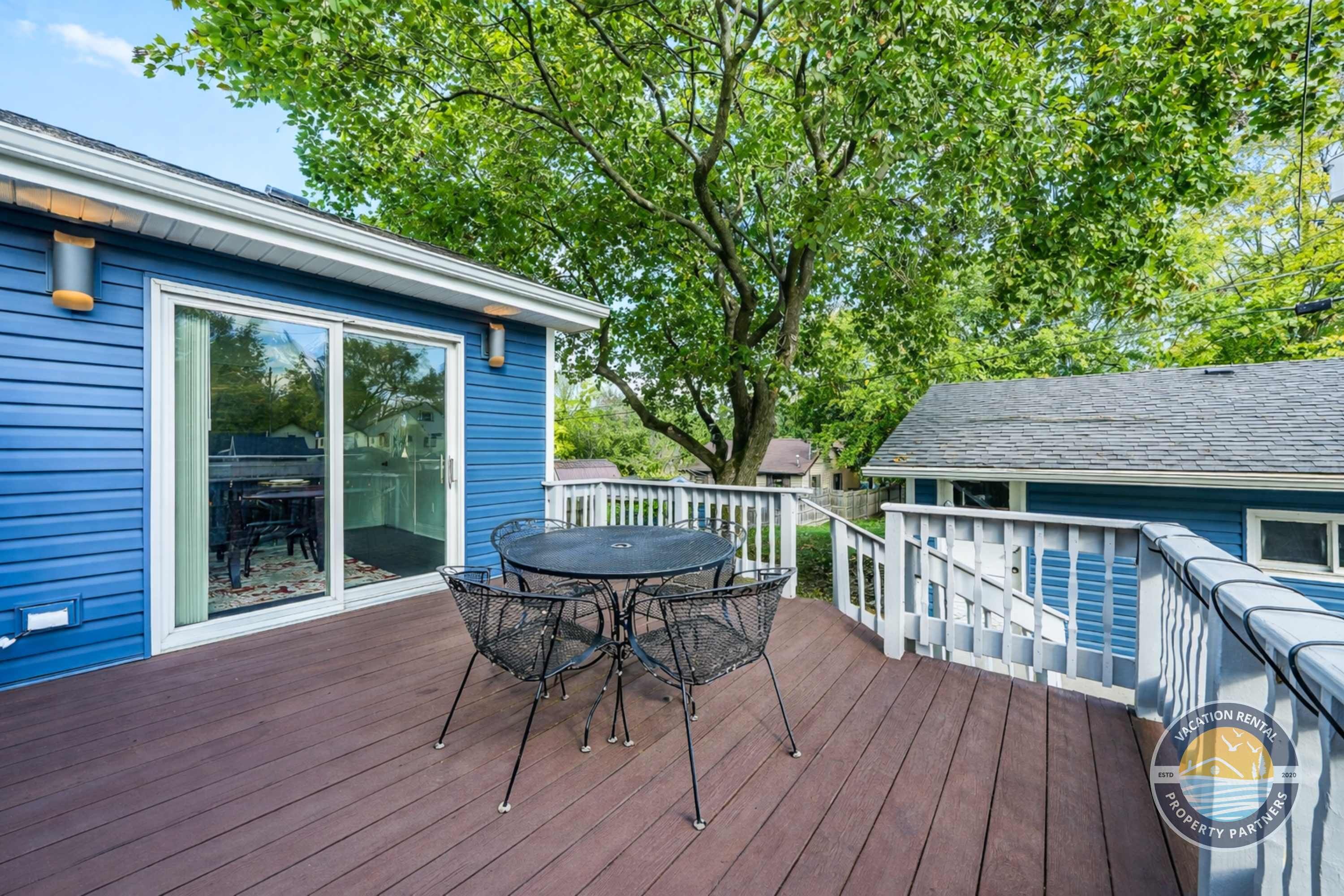 A blue house with a deck, a table with chairs, and a large tree.