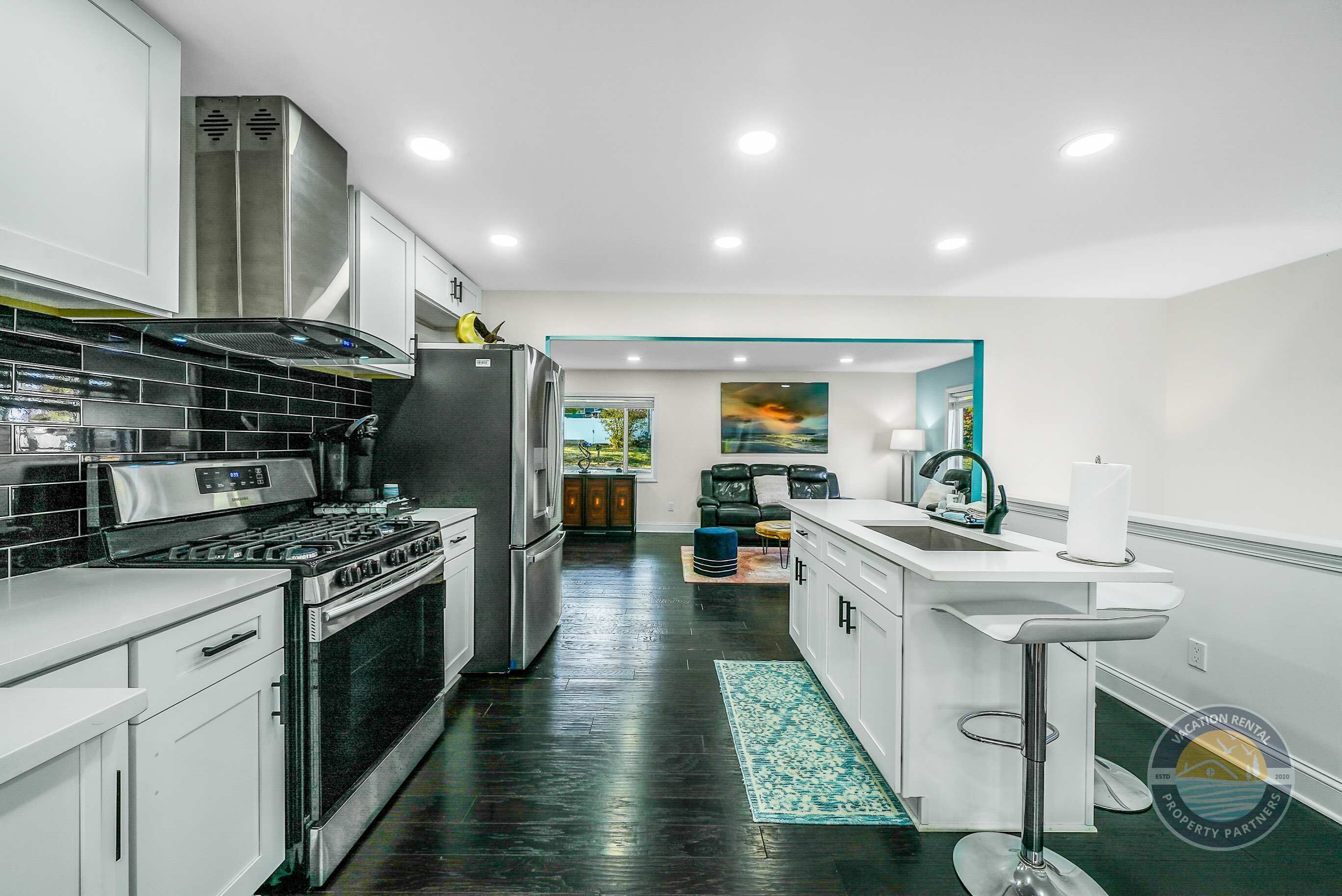 Una cocina moderna con electrodomésticos de acero inoxidable, un salpicadero de azulejos negros y un piso de madera oscura.