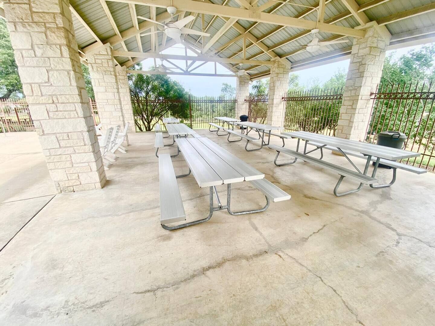 A covered picnic area with stone pillars, metal picnic tables, and a metal fence.