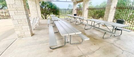 A covered picnic area with stone pillars, metal picnic tables, and a metal fence.