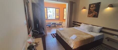 A hotel room with a bed, a desk, a chair, a TV, and a painting on the wall.