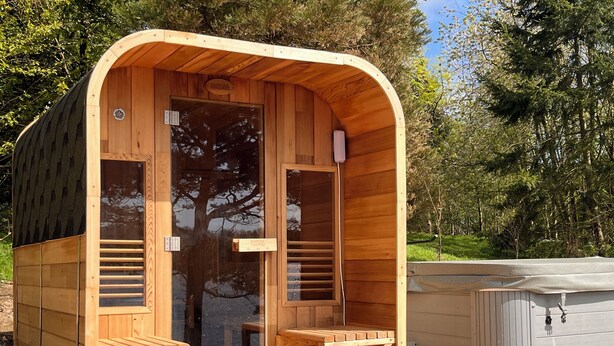 Un sauna en bois avec une porte en verre, un petit banc en bois et un jacuzzi.