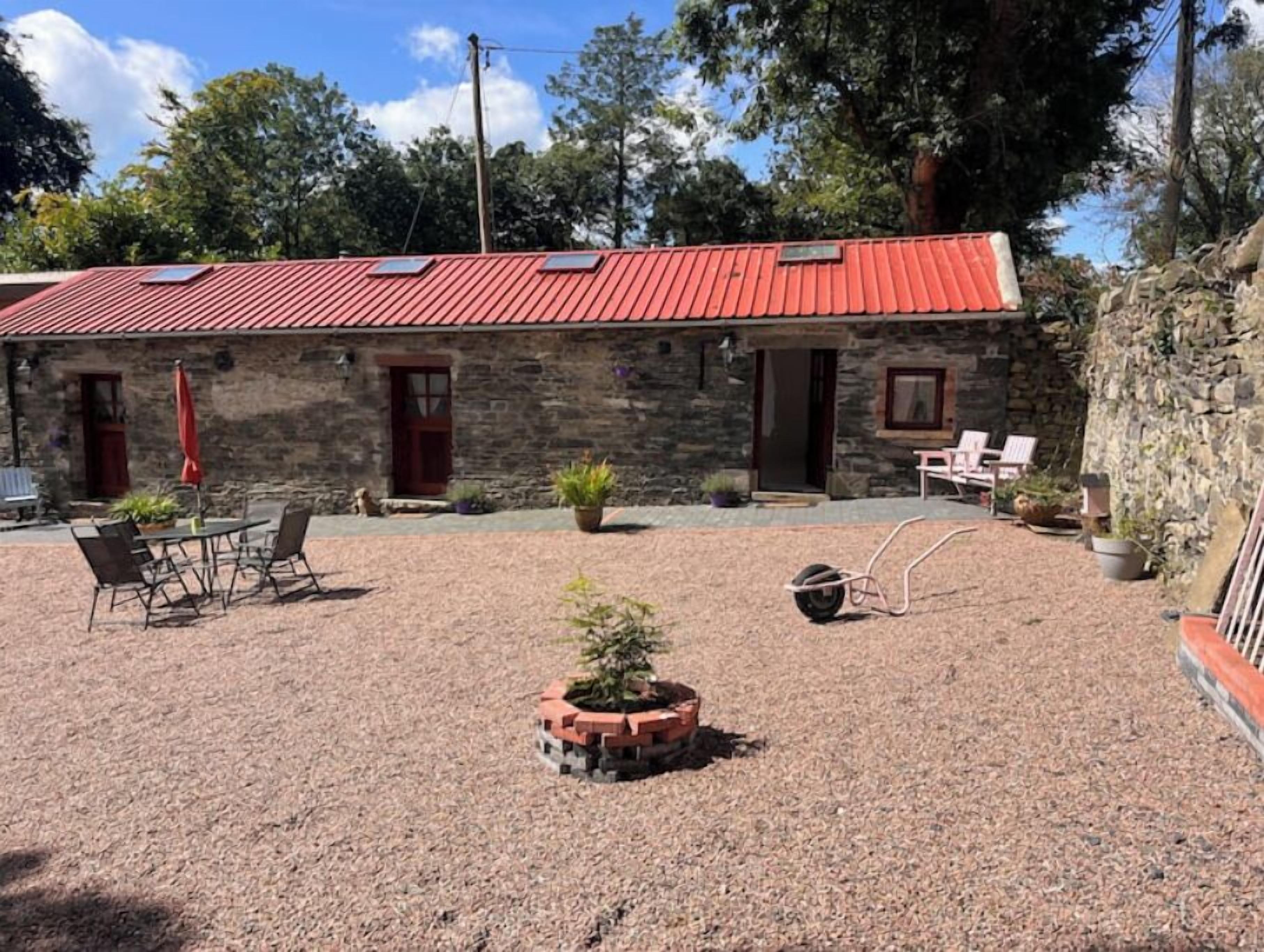 Un edificio de piedra con techo rojo, mesas al aire libre y un patio de grava.