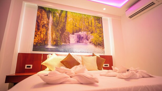 A hotel room with a large wall mural of a waterfall, a neatly made bed with pillows, and a bedside table. - J60 Suites (New Delhi)