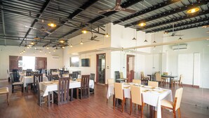 A spacious dining area with multiple tables and chairs, ceiling fans, and pendant lights. - J60 Suites (New Delhi)