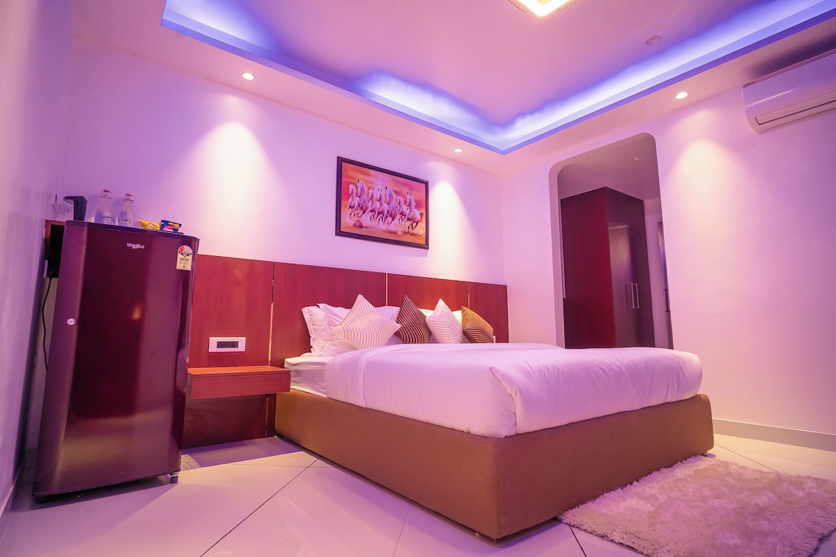 A modern bedroom with a large bed, a wardrobe, a nightstand, and a ceiling light fixture.