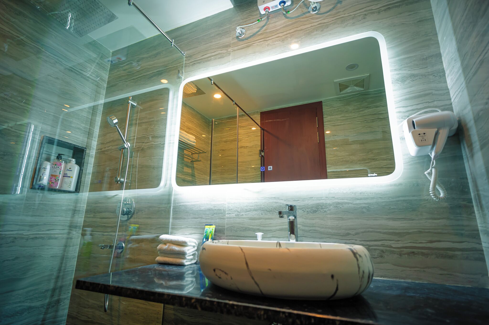 A modern bathroom with a large mirror, a round sink, and a handheld showerhead.