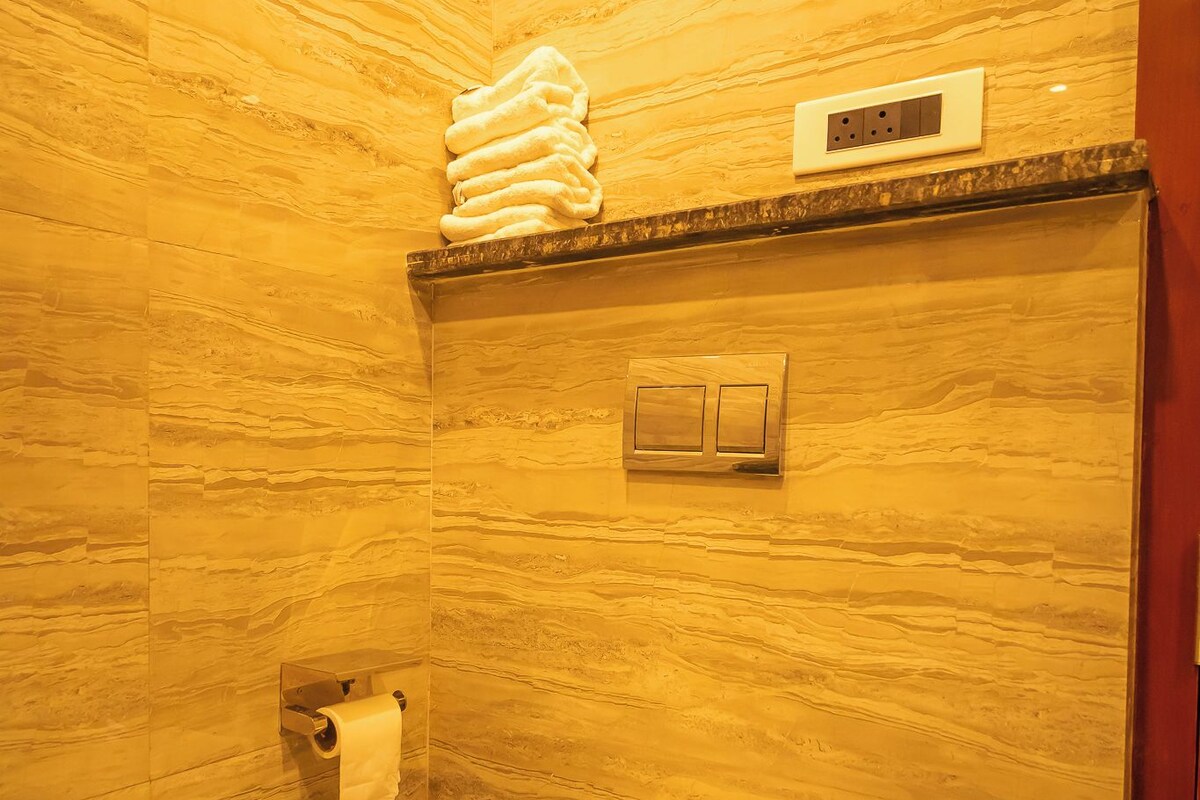 A bathroom with a toilet, a trash bin, a towel rack, and a wall-mounted electrical outlet.