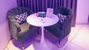 A room with two green armchairs, a white round table, and a purple curtain backdrop. - J60 Suites (New Delhi)