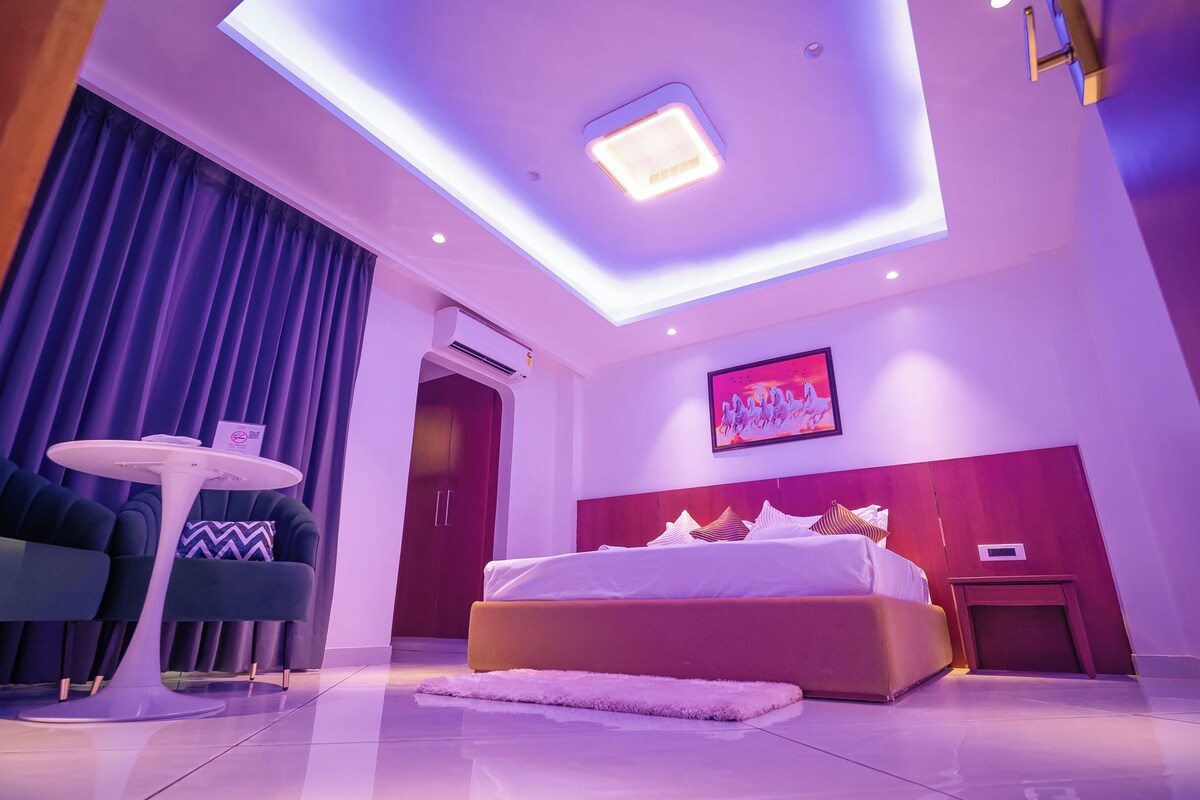 A modern hotel room with a large bed, a round table, and a ceiling light.