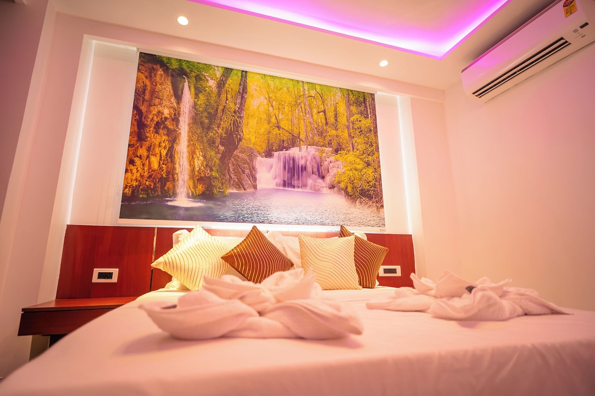 A hotel room with a large wall mural of a waterfall, a neatly made bed with pillows, and a bedside table.