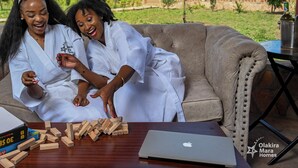 Two people sitting on a couch with a laptop and wooden blocks on a table. - Olakira Mara Homes (Maasai Mara)